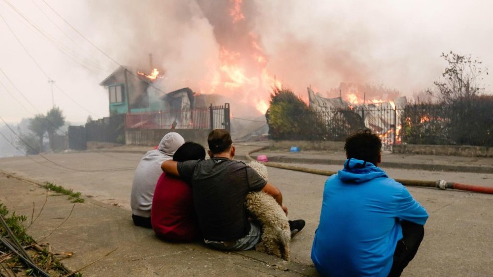 Membros de uma família observam sua casa afetada pelos incêndios florestais em Penco, Chile, em 18 de janeiro de 2026. Um total de 16 pessoas morreram em diversos incêndios florestais que ainda queimam no sul do Chile, nas regiões de Nuble e Biobío, conforme relatado pelo Ministro da Segurança Pública, Cordero. EPA/PABLO HIDALGO