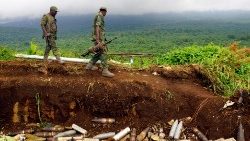 Congolese military personnel walk past an armoury site used by M23 rebels