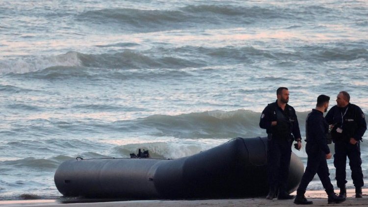 French policemen stand beside a dinghy lying on the beach after migrants tried to reach Britain