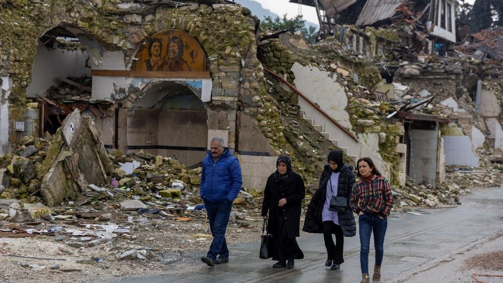 Pessoas passam por casas destruídas pelo terremoto do ano passado, em Hatay, Turquia, em 5 de fevereiro de 2024. O tremor de magnitude 7,8 que ocorreu nas primeiras horas de 6 de fevereiro de 2023 arrasou vilas e áreas urbanas no sudeste do país. Matou mais de 53 mil pessoas na Turquia e quase 6 mil na vizinha Síria e deixou milhões de desabrigados. REUTERS/Umit Bektas