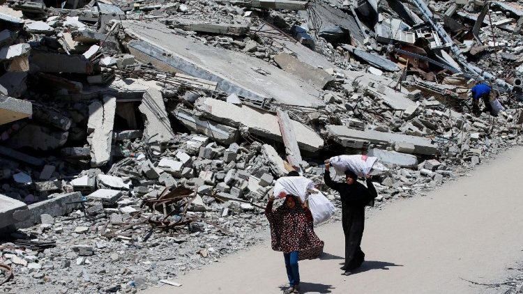Palestinian woman and a girl carrying bags of firewood walk by the rubble of houses, in Gaza