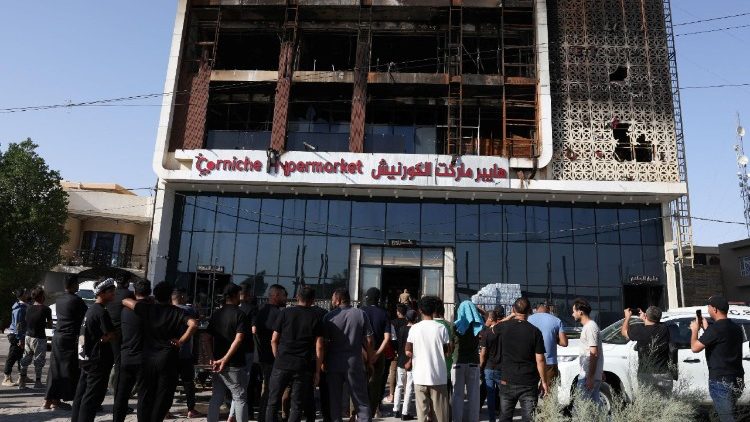 People gather outside the burnt out remains of the shopping centre that was destroyed in a fire on 16 July