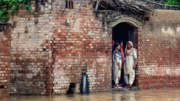 Residents stand at the entrance of a house on a flooded road, caused by monsoon rains and the rising water level of the Sutlej River, in Hakuwala village near the Pakistan-India border