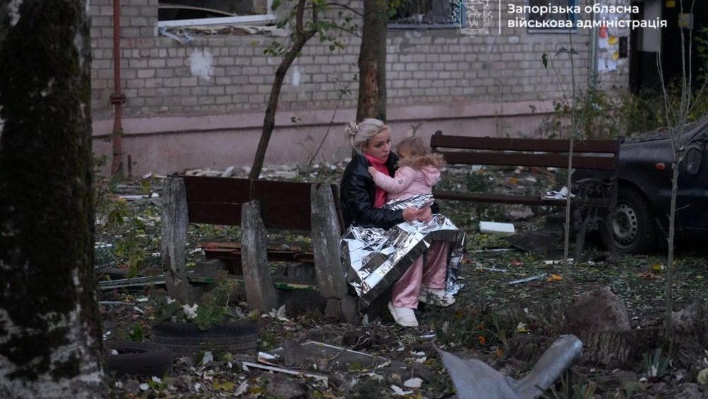Uma moradora segura uma criança pequena coberta com um cobertor térmico em frente a um dormitório danificado durante ataques noturnos com mísseis e drones russos, em meio ao ataque da Rússia à Ucrânia, em Zaporizhzhia, Ucrânia, em 30 de outubro de 2025. Serviço de imprensa da Administração Militar Regional de Zaporizhzhia/Divulgação via REUTERS.