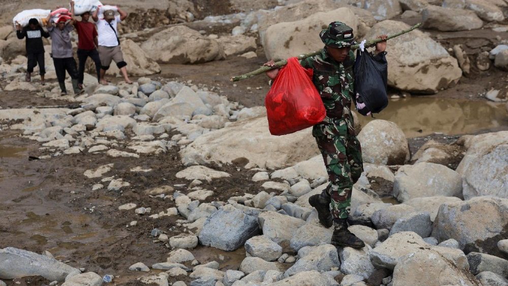 Um soldado, acompanhado por moradores locais, carrega suprimentos de socorro para serem distribuídos às pessoas em uma área atingida por enchentes repentinas e mortais após fortes chuvas em Palembayan, distrito de Agam, província de Sumatra Ocidental, Indonésia, em 2 de dezembro de 2025. REUTERS/Willy Kurniawan