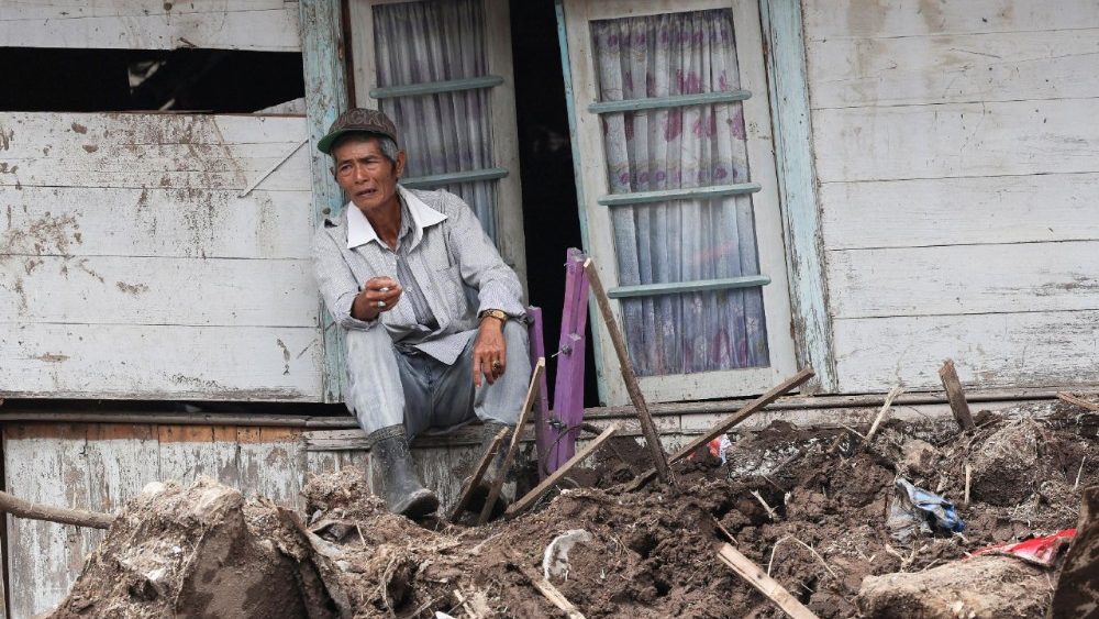 Um homem está sentado no parapeito da janela de uma casa gravemente danificada após deslizamentos de terra mortais causados ​​por fortes chuvas em Malalak, distrito de Agam, província de Sumatra Ocidental, Indonésia, em 3 de dezembro de 2025. REUTERS/Willy Kurniawan