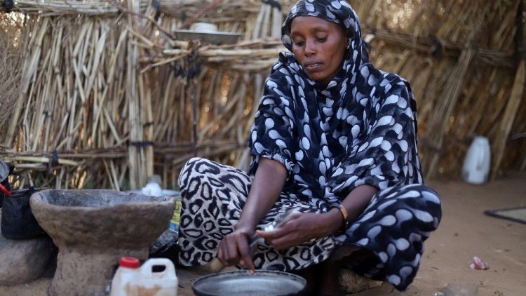 A displaced Sudanese mother of four, prepares food at a camp shelter amid the ongoing conflict
