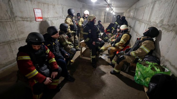 Equipes de resgate e bombeiros se abrigam enquanto trabalham no local de um centro de log&iacute;stica de uma empresa privada de entregas atingido por um ataque de m&iacute;ssil russo, em meio ao ataque da R&uacute;ssia &agrave; Ucr&acirc;nia, em Kharkiv, Ucr&acirc;nia, em 13 de janeiro de 2026. REUTERS/Sofiia Gatilova