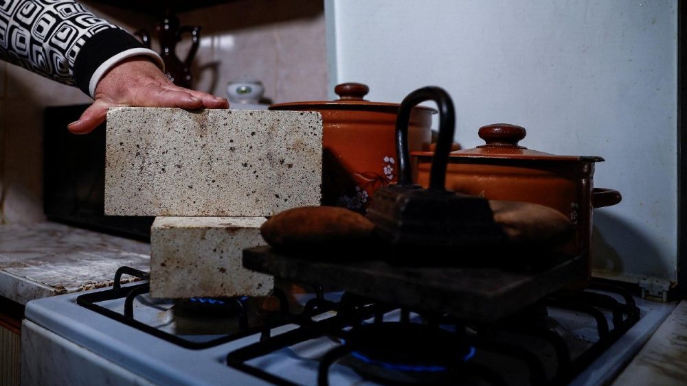 Liubov Klymenko, de 66 anos, verifica se um tijolo refratário aqueceu o suficiente em seu fogão a gás, que ela usa junto com pedras e um ferro de passar roupa antigo da família para aquecer seu apartamento após infraestruturas civis críticas terem sido atingidas por recentes ataques de mísseis e drones russos, em meio ao ataque da Rússia à Ucrânia, em Kiev, Ucrânia, 23 de janeiro de 2026. REUTERS/Alina Smutko