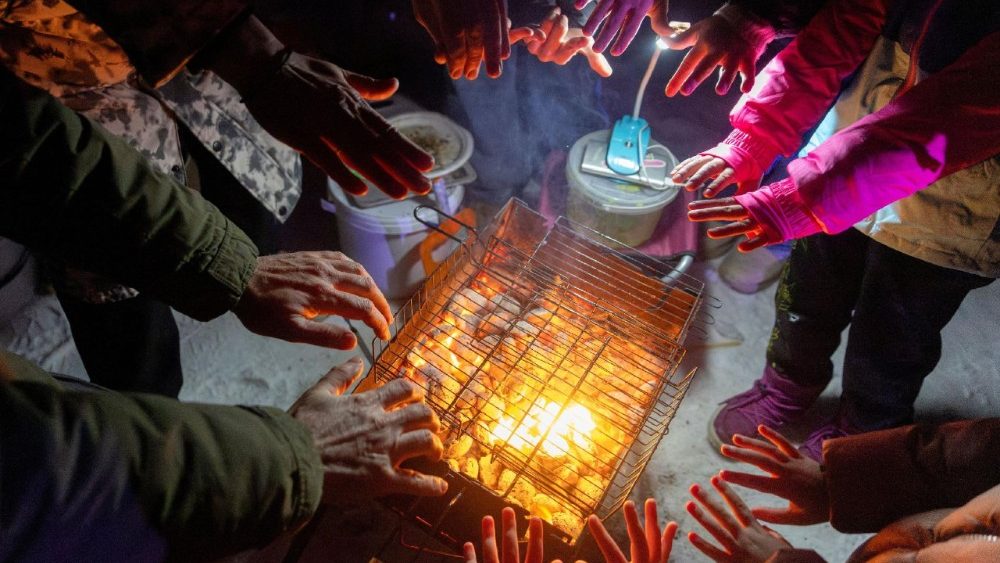 Pessoas aquecem as mãos em uma churrasqueira durante uma festa em um campo esportivo em um bairro que ficou sem energia elétrica após recentes ataques russos à infraestrutura civil da capital, em meio ao ataque da Rússia à Ucrânia, em temperaturas abaixo de zero em Kiev, Ucrânia, em 24 de janeiro de 2026. A festa foi organizada por um DJ local que disse que as pessoas preferiam dançar com seus vizinhos na rua do que ficar em seus apartamentos frios e escuros para animar o ambiente durante os frequentes cortes de energia e aquecimento. REUTERS/Thomas Peter