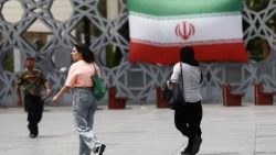 Einige Menschen laufen in Teheran neben einer Wand mit der Darstellung der iranischen Fahne