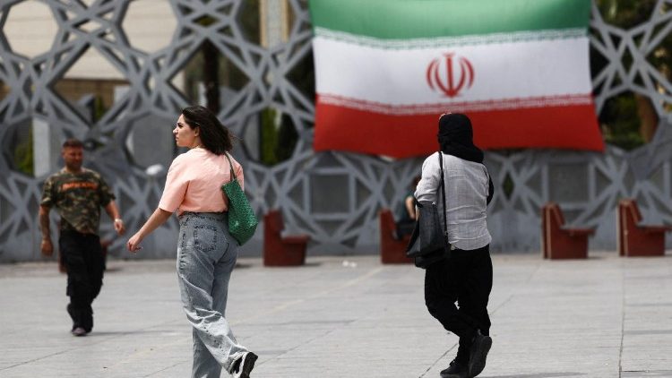 Einige Menschen laufen in Teheran neben einer Wand mit der Darstellung der iranischen Fahne