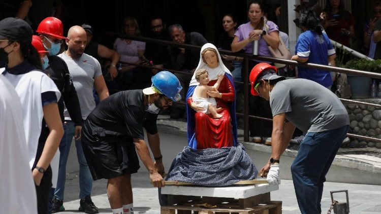 Varias personas transportan una estatua religiosa de la Virgen con el Ni&ntilde;o cerca del lugar donde se encontraba un edificio da&ntilde;ado tras los terremotos.