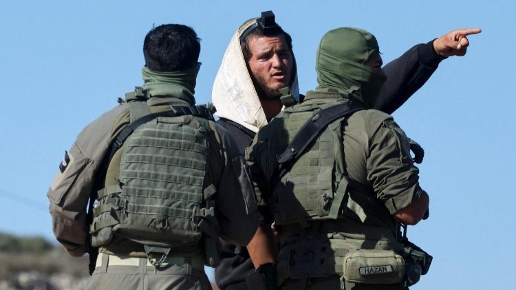Israeli soldiers speak to an Israeli settler who entered Palestinian-American Loui Ridi's property, in Qusra