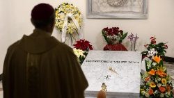 Sacerdote reza diante do túmulo de Bento XVI no primeiro aniversário de seu falecimento.