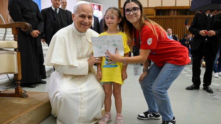 Pope Leo XIV bends down to take a photo with a girl taking part in the Vatican summer camp