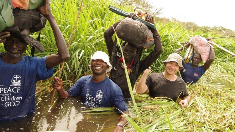 Comboni Patres Gregor und Alfred mit Katecheten waten durch überschwemmtes Gelände zu den Kapellen