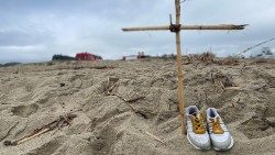 a pair of shoes and a makeshift cross on the beach of Cutro