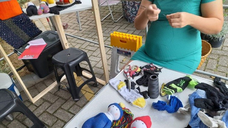 A pregnant woman stitches clothes for two dolls