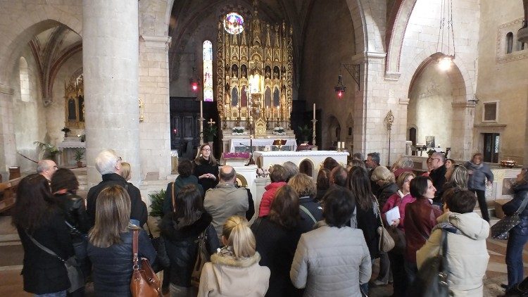 Pellegrini e turisti all'interno della basilica di Santa Maria di Follina (Treviso): alle spalle dell’altare si vede la pala lignea che accoglie la statua in arenaria della Madonna del Sacro Calice,