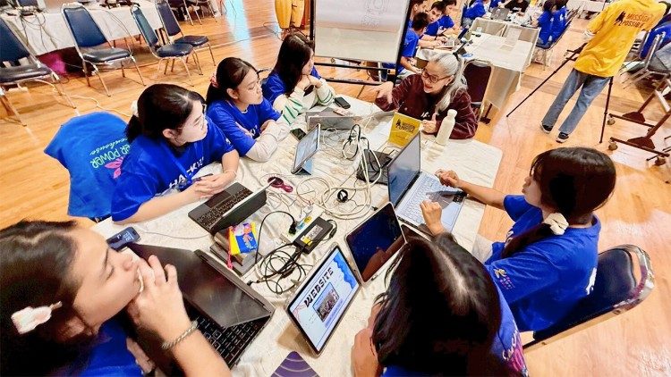 A team of student hackers collaborates with their pitching coach during an intensive hacking session at MISSION POSSIBLE Youth Social Hackathon Season 2, held at Baan Phu Waan Pastoral Training Center, Thailand, July 2025.