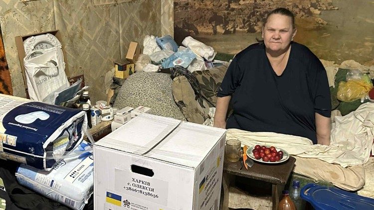 Žena přebírá balíček s potravinami, dar od papeže, ve svém domě