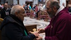 Fra Agnello Stoia consegna una croce da appendere in una nuova casa ottenuta dopo una vita in strada