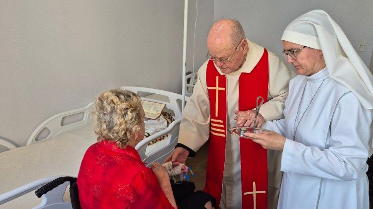 Padre Belmiro administrando a unção dos enfermos a uma idosa, acompanhado por uma Pequena Missionária